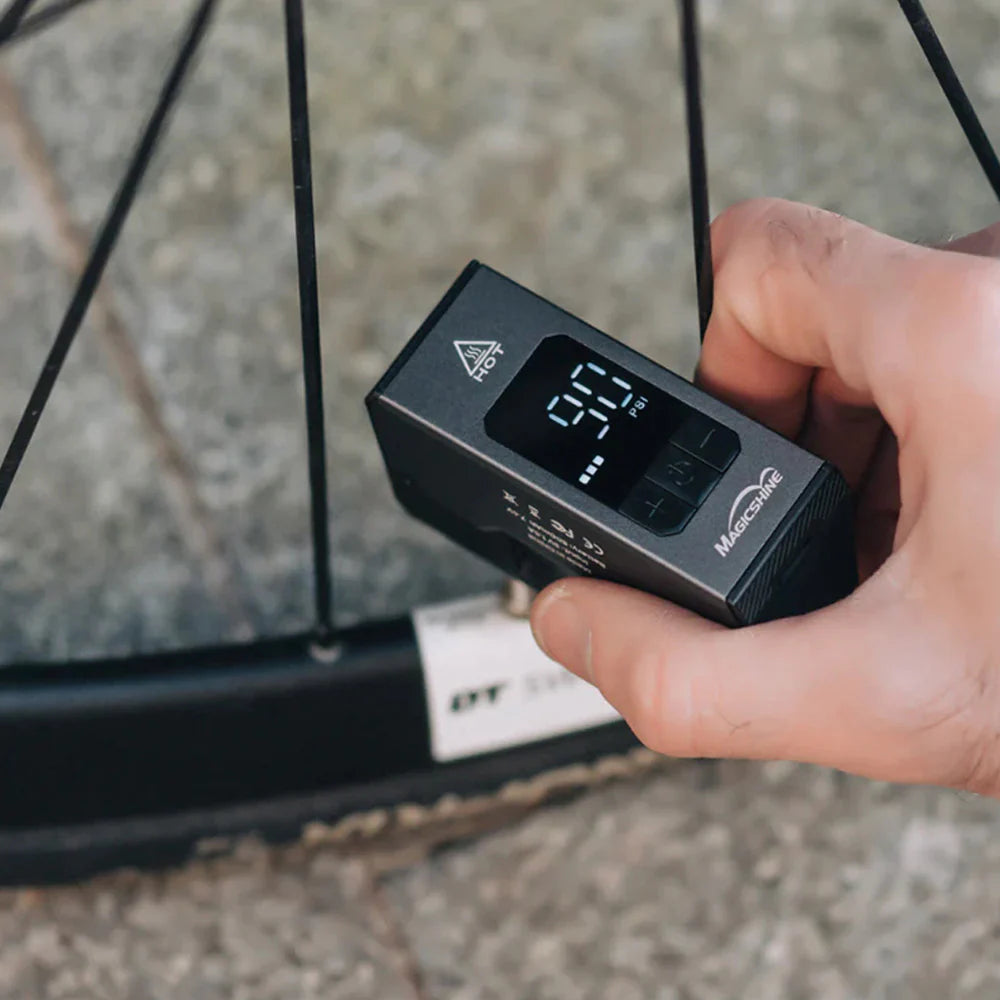 Magicshine Airro E‑Pump digital tyre pressure gauge in front of a bicycle wheel.