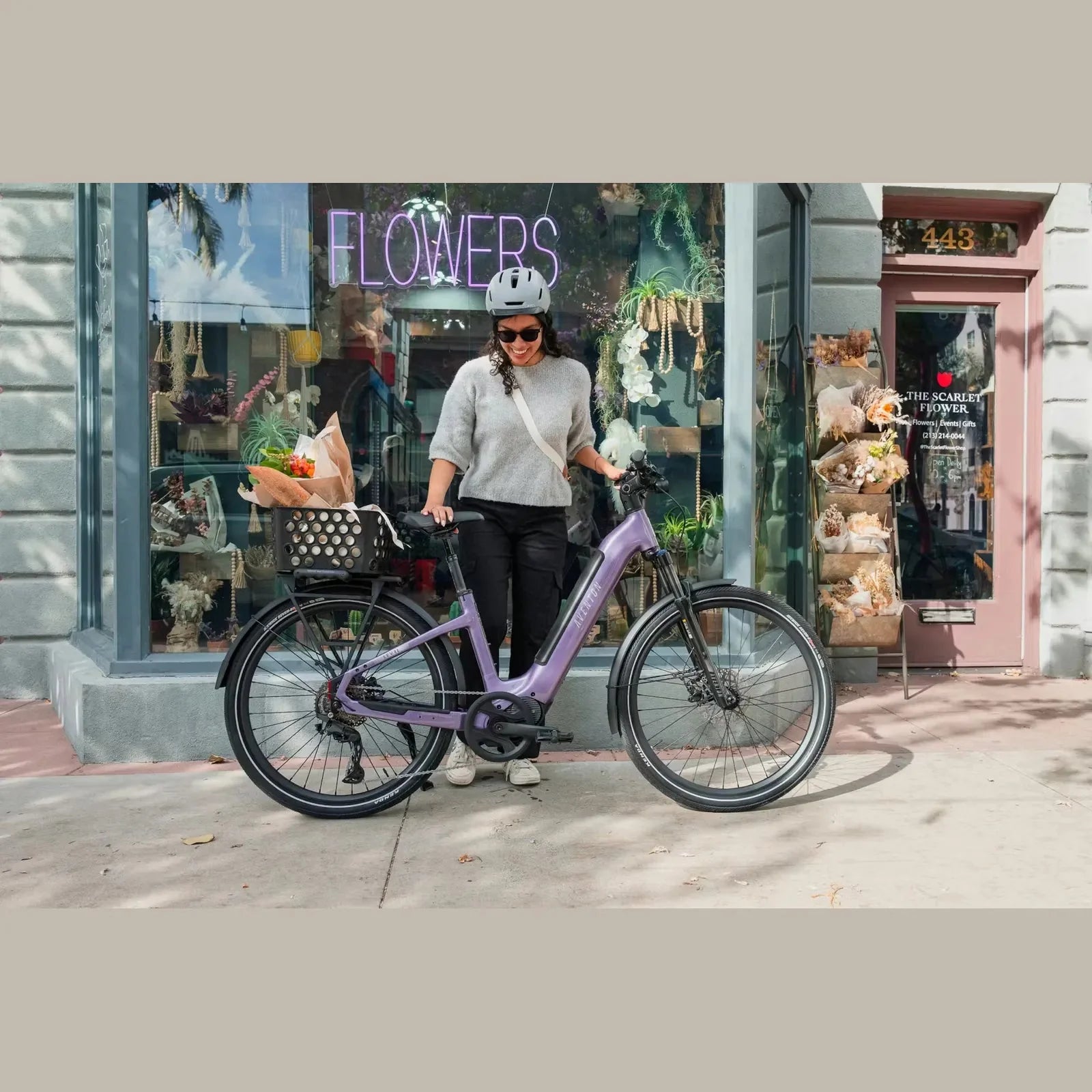 Person with a purple Aventon Trava ADV electric bike in front of a store with a 'Flowers' sign.