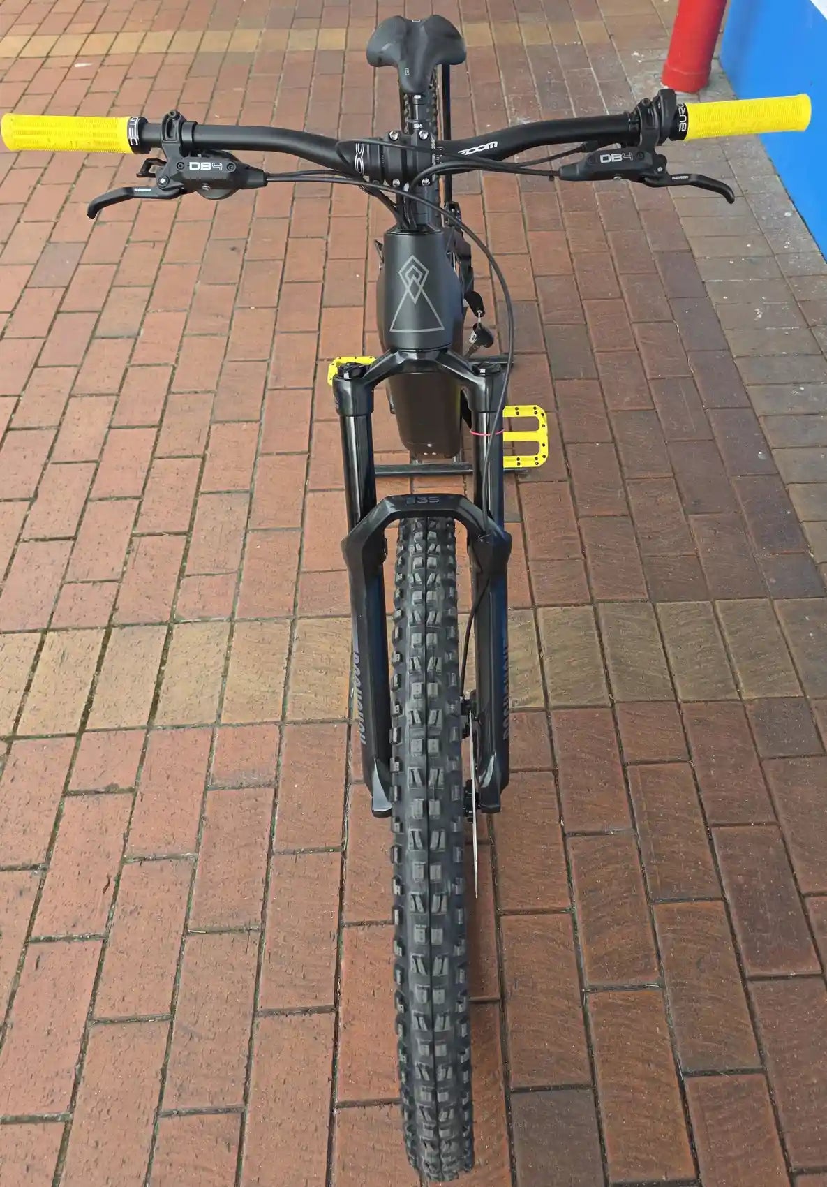 Black bicycle with yellow handlebars on a brick pavement
