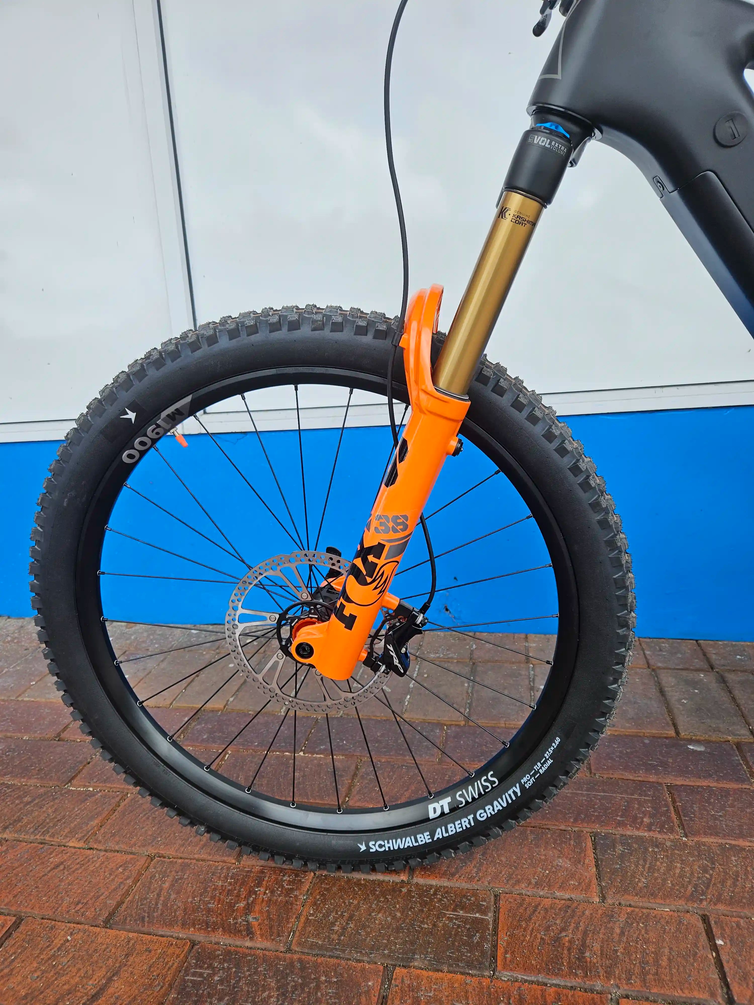 Close-up of a Rhyolite bicycle wheel with orange Fox 38 suspension fork against a blue and gray background