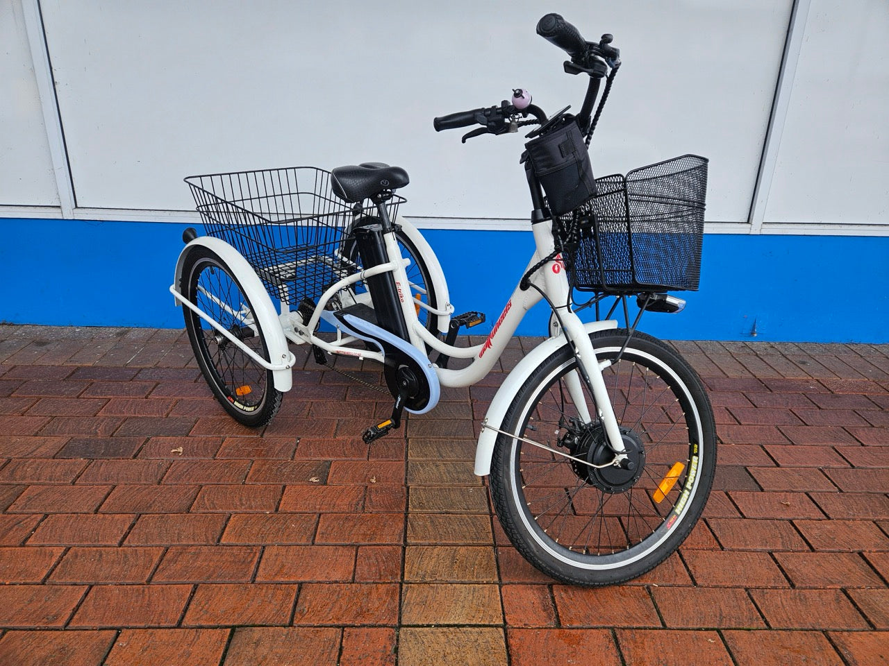White electric tricycle with baskets on a brick pavement