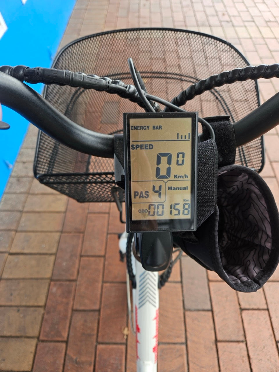 Bicycle speedometer attached to a bike handlebar with a basket on a brick pavement.