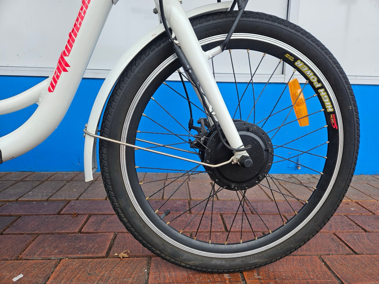 Close-up of a bicycle wheel with visible gear and chain on a brick pavement.
