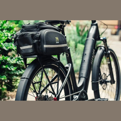 Black Aventon Trava ADV Step Through City E-Bike with trunk bags on a blurred natural background