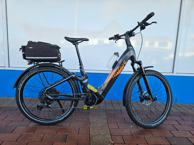 Electric bicycle with a black bag on a brick pavement against a blue and white wall.