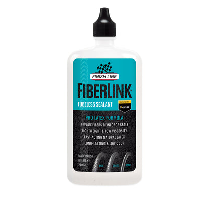 A bottle of Finish Line Fiberlink Pro Latex Tubeless Tyre Sealant in a clear plastic bottle with a black cap. The label includes the product name and features, such as 'Kevlar fibers', 'Pro latex formula', and 'Low odor'.