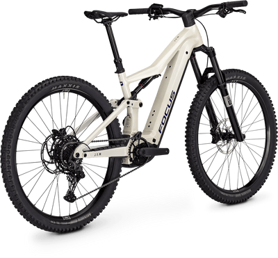 A full-suspension electric mountain bike with a cream-colored frame and black components, including the fork, wheels, tires, and handlebars. The frame features the 'FOCUS' brand name in dark gray lettering.