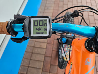 Close-up of a bicycle handlebar with a digital speedometer on a tiled pavement background