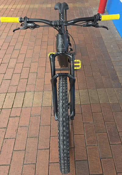 Black bicycle with yellow handlebars on a brick pavement