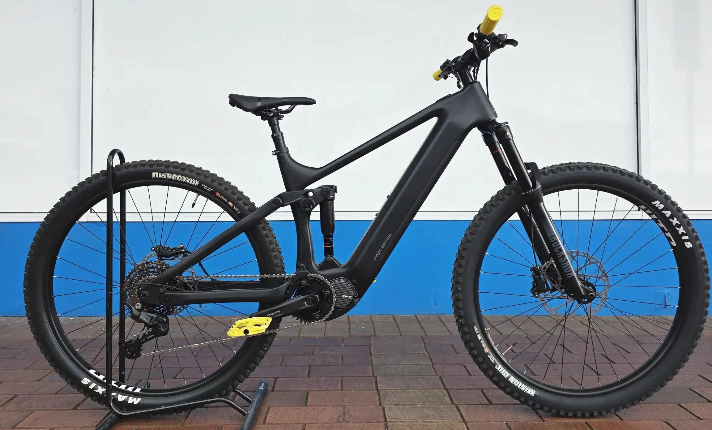 Black electric bike on a stand against a white and blue wall.