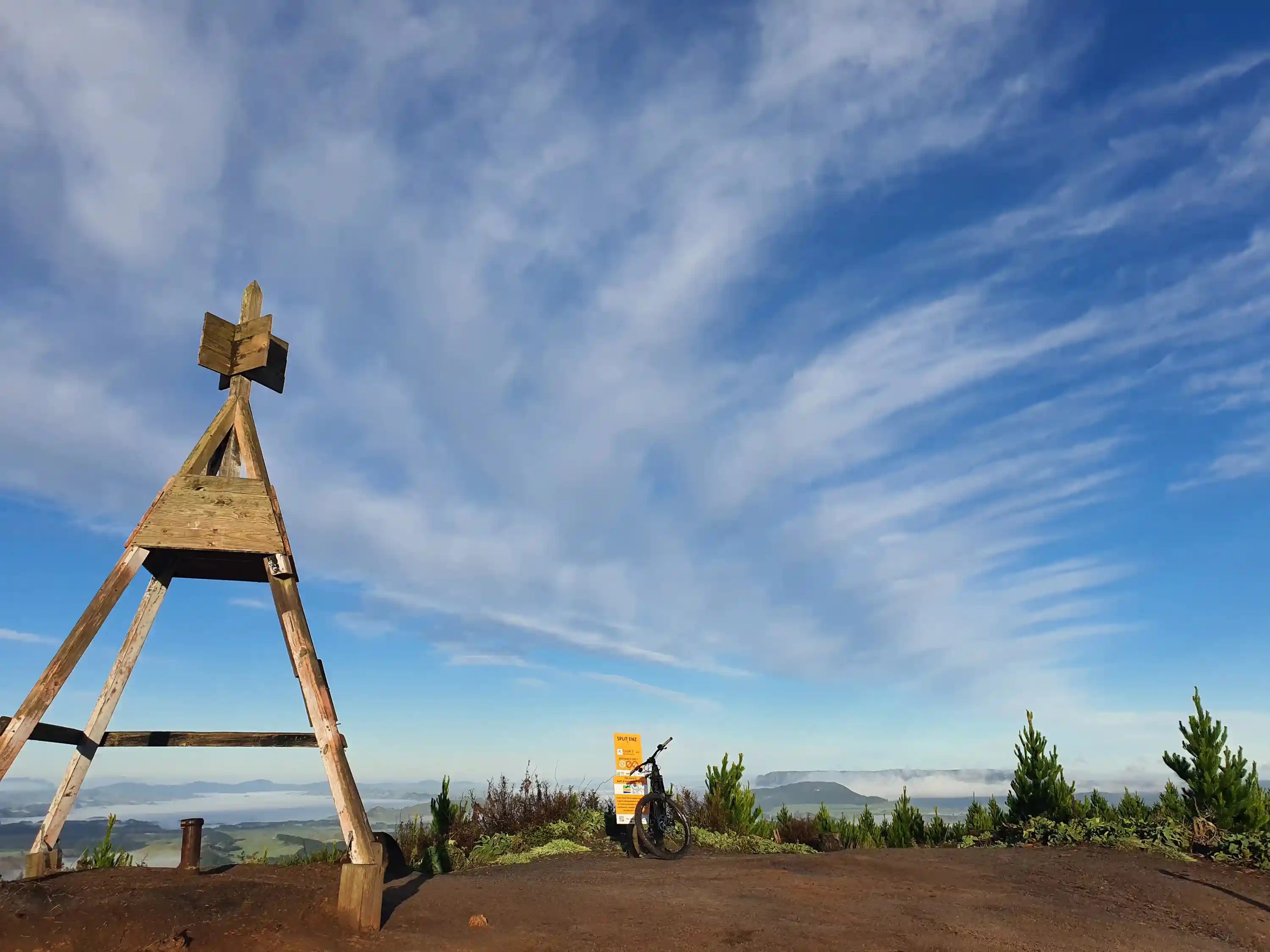 Wooden structure, trig, on a hilltop of Split Enz MTB trail with a scenic view and blue sky.