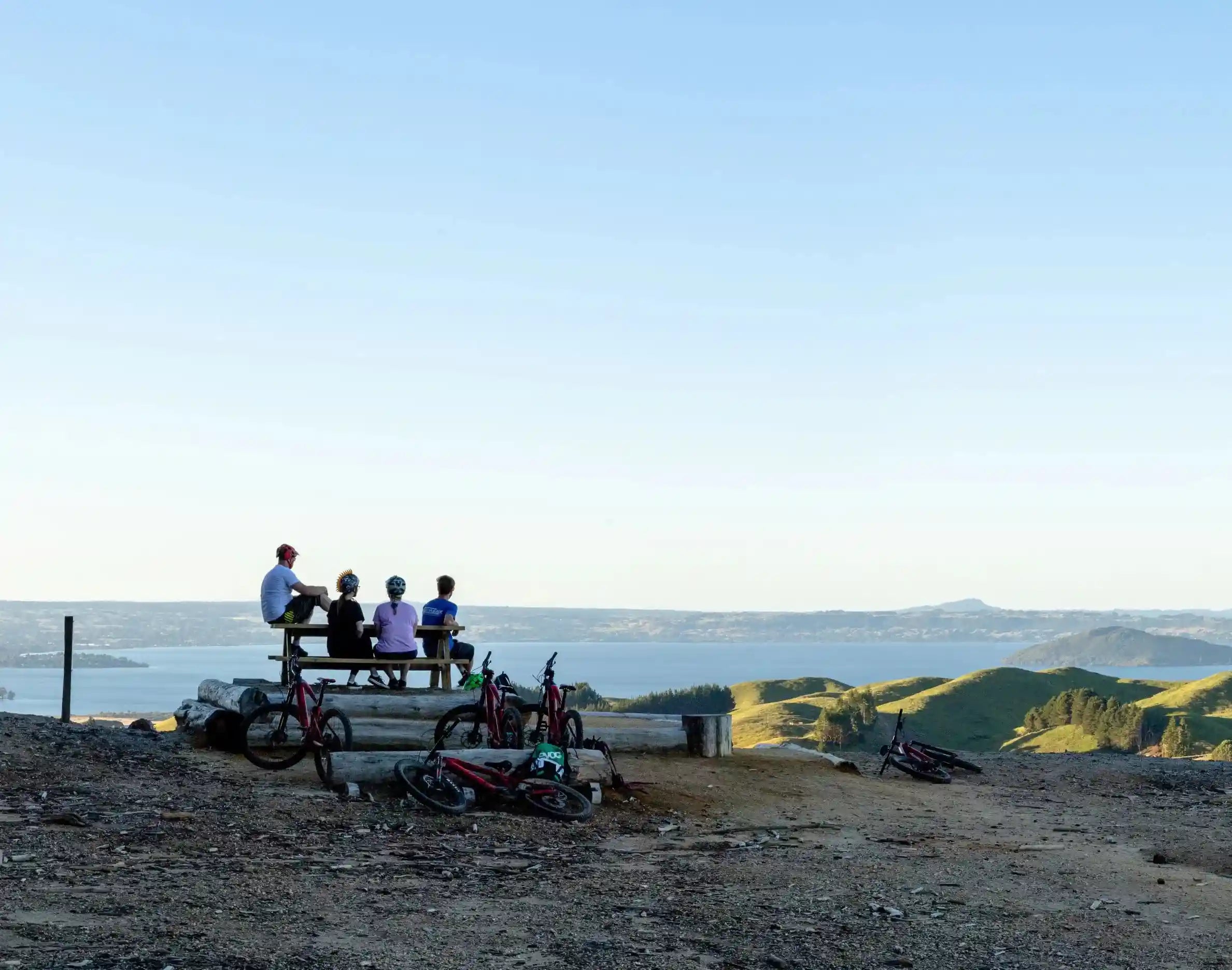 Group of people sitting on a picnic table at with bicycles at a scenic overlook Lake Rotorua. 