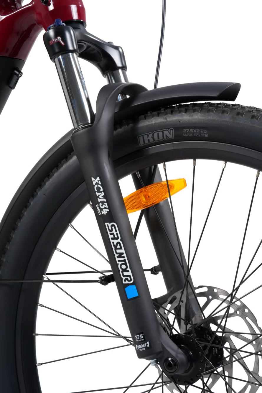 Close-up of a bicycle front wheel and suspension fork, showing a black knobby tire with an orange reflector and a black fork branded SCM with a blue accent.