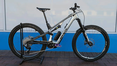 A full-suspension Whyte Ex-demo with a silver and black frame, displayed on a black stand against a blue and white wall.