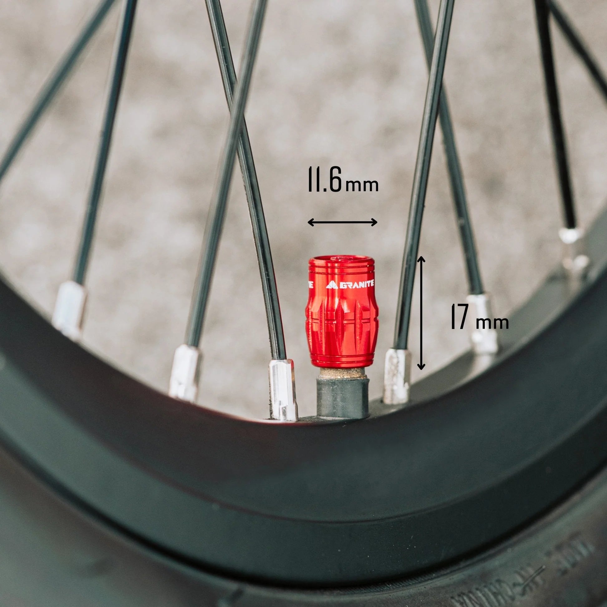 Close-up of a bicycle wheel with a red valve cap labeled '11.6 mm' and '17 mm'.
