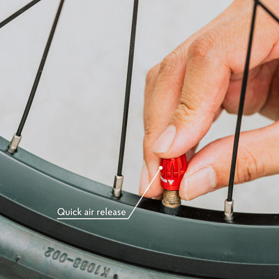 Person inflating a bicycle tire with a red valve, focusing on the quick air release feature.