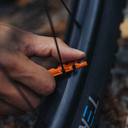 Hand adjusting an orange tool on a bicycle wheel with 'Kona' branding.
