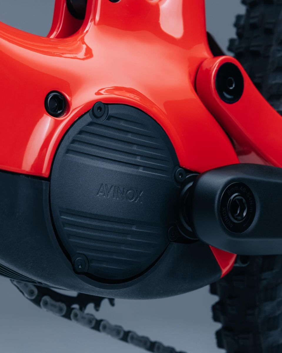 Close-up of AVINOX motor system on Steppenwolf Tundra 9, showing the engine casing, chain guard, and part of the tire against a neutral gray background.