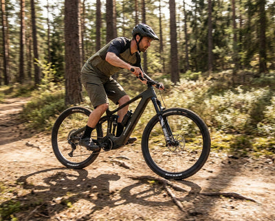 A man riding a steppenwolf Tundra electric mountain bike on a dirt trail in a dense pine forest. 